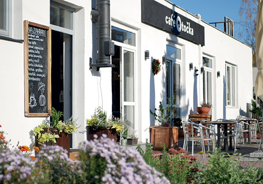 Kavárna Café Otočka zvenčí s tabulí s nabídkou a květinami před vchodem